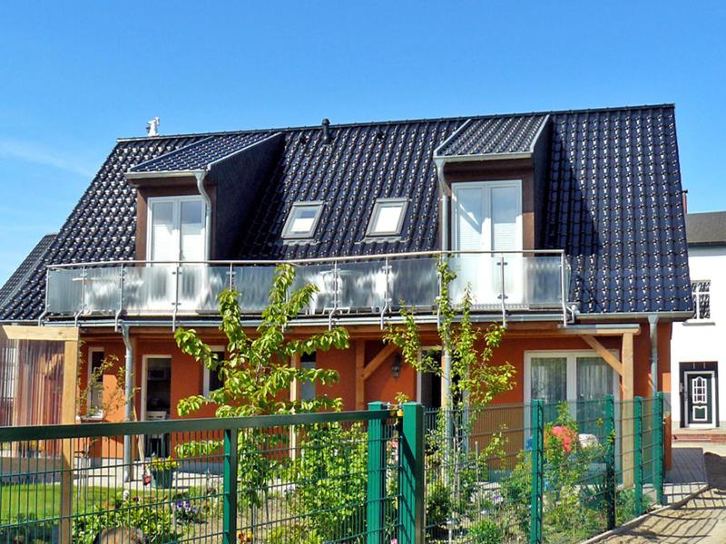 ein Haus mit einem schwarzen Dach und einem Zaun in der Unterkunft Ferienwohnungen mit Balkon in Kröslin