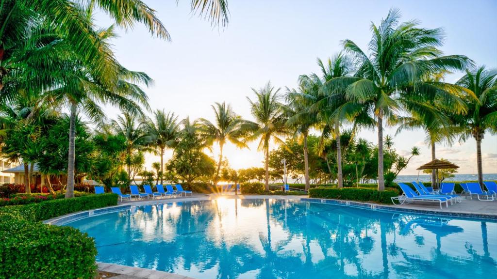 a swimming pool with palm trees and chairs and the ocean at 409 Mariners Club in Key Largo