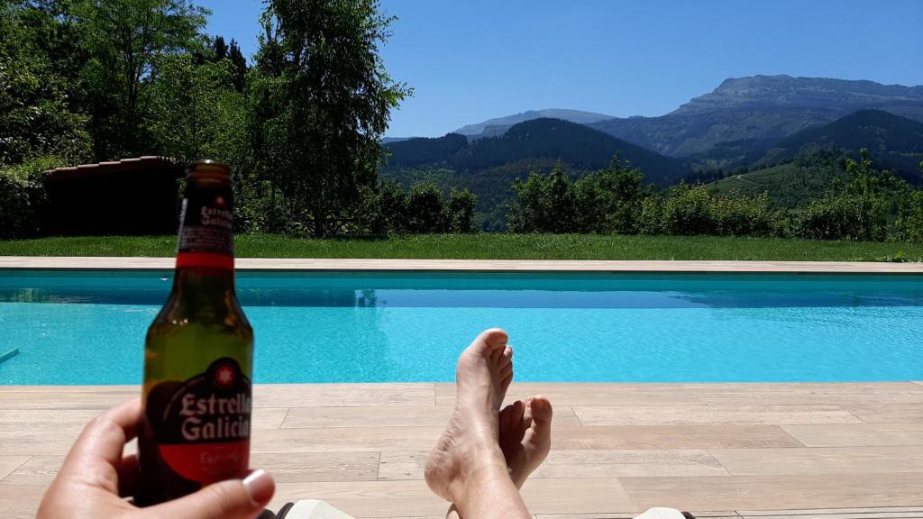 a person holding a bottle of beer next to a swimming pool at ITURRIOTZ BEREZIA in Areatza