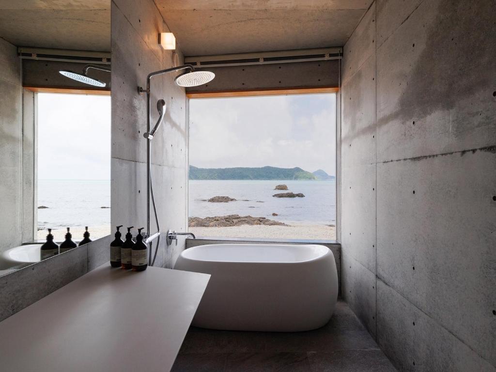 a bathroom with a tub and a large window at Denpaku The Beachfront MIJORA in Amami