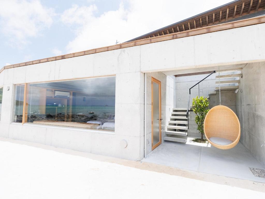 a white building with a large window and a chair at Denpaku The Beachfront MIJORA in Amami
