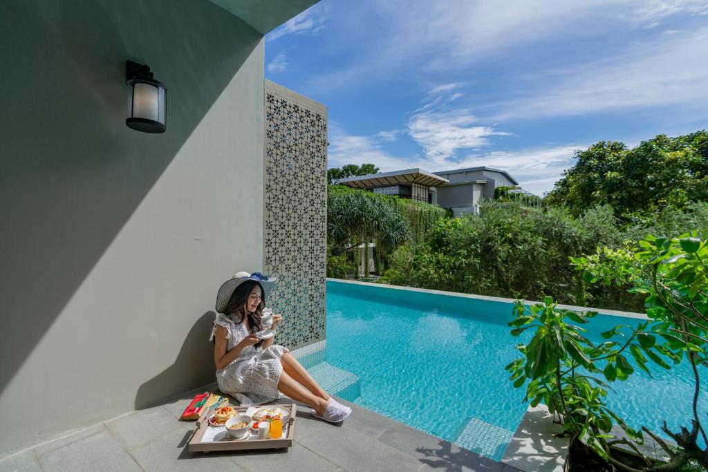 a woman in a dress sitting next to a swimming pool at Proud Phuket Hotel, Naiyang Beach in Nai Yang Beach