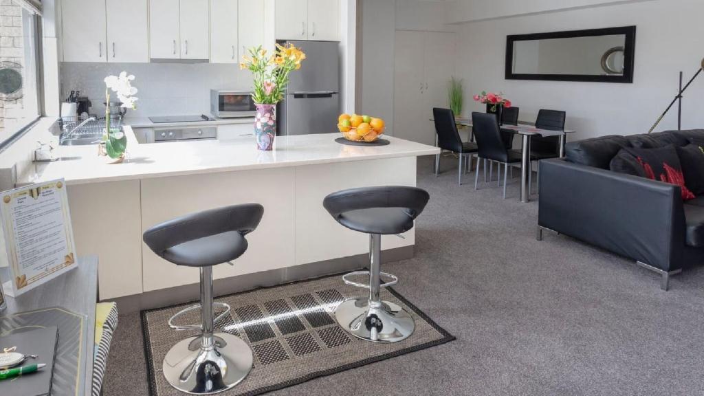 a kitchen with two bar stools and a living room at central park boutique apartment in Armidale