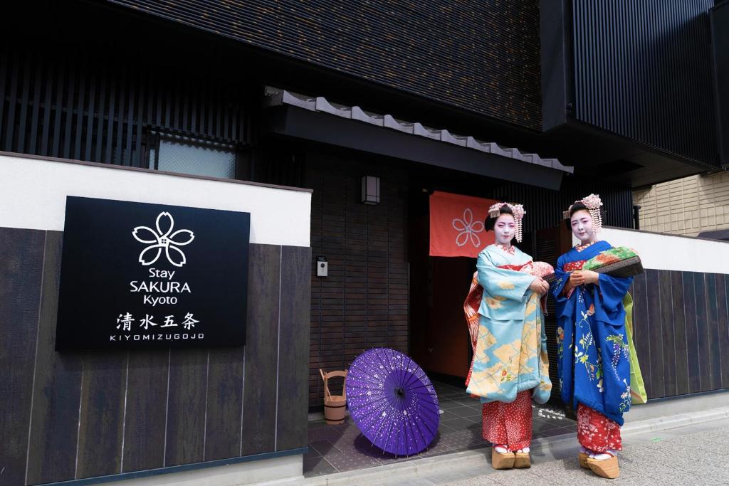 dos personas en kimonos parados frente a un edificio en Stay SAKURA Kyoto Kiyomizu Gojo, en Kioto