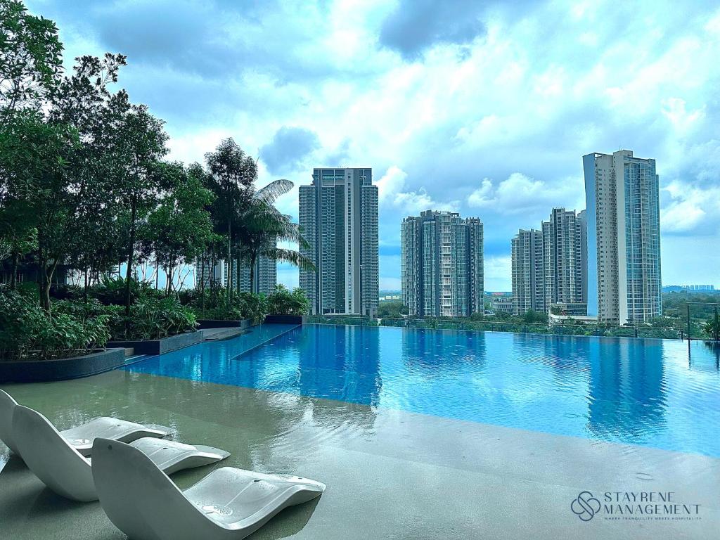 a large swimming pool with white chairs in front of a city at The Elysia Suites in Nusajaya