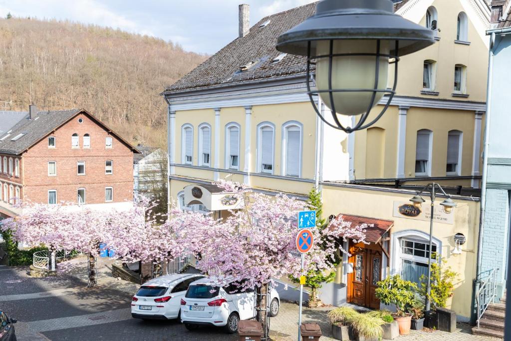 a street with cars parked next to a building with a flowering tree at Hotel Royal in Betzdorf