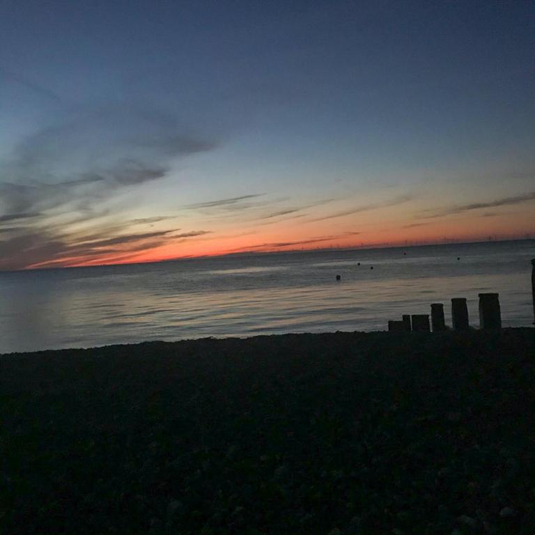 a sunset on the beach with people in the water at The Bubble Hideaway - A Little Oasis near the Sea in Whitstable