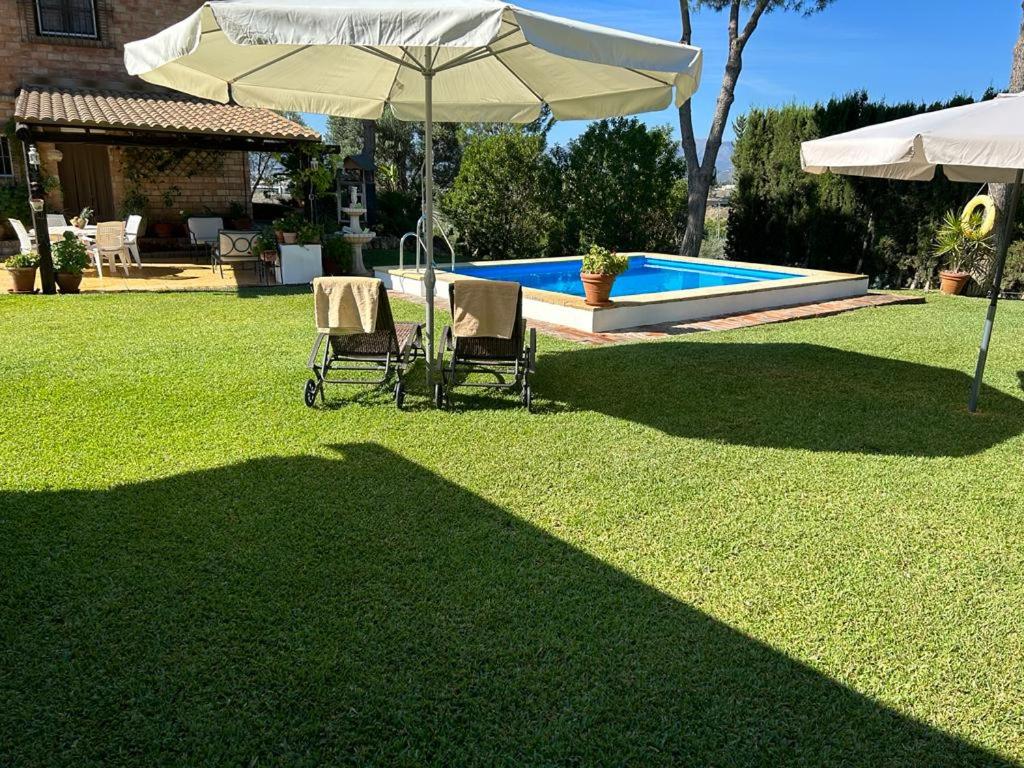 two chairs and an umbrella in a yard with a pool at Casa Rural Cupiana Piscina privada Malaga in Málaga