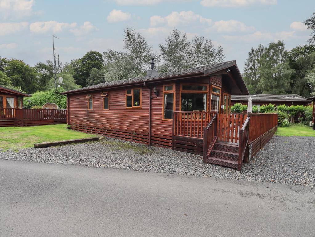 a large wooden cabin with a porch on a gravel road at Langdale Lodge 15 in Windermere