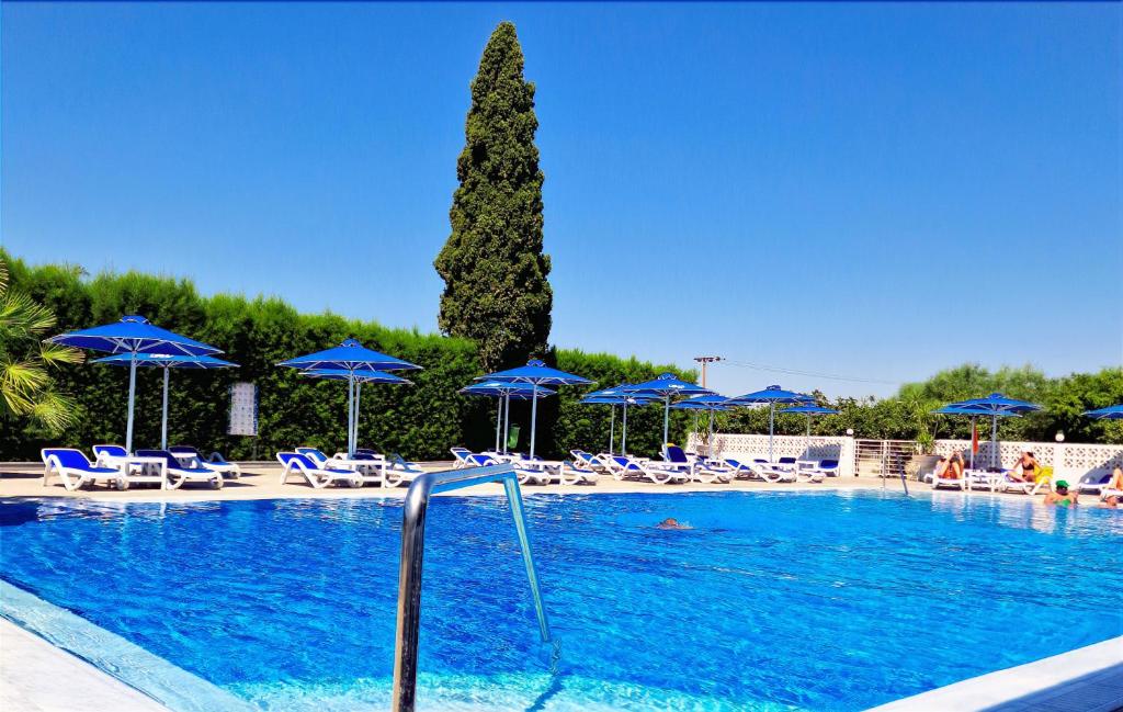 einen Pool mit Stühlen und blauen Sonnenschirmen und einem Baum in der Unterkunft Sveltos Hotel in Larnaka