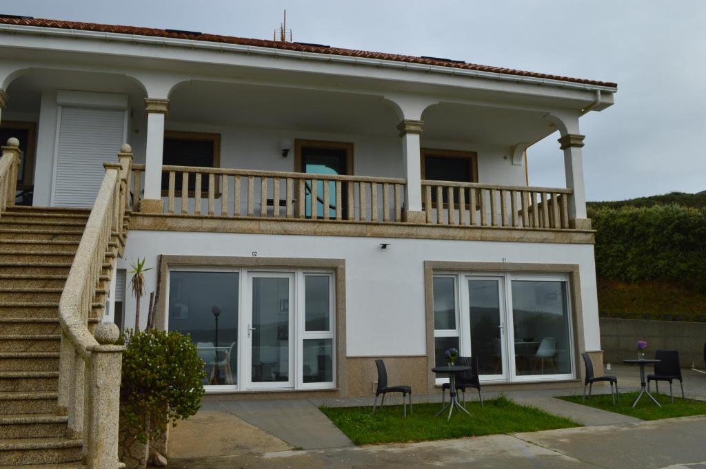 uma grande casa branca com uma varanda e cadeiras em Apartamentos Playa de Nemiña em Nemiña