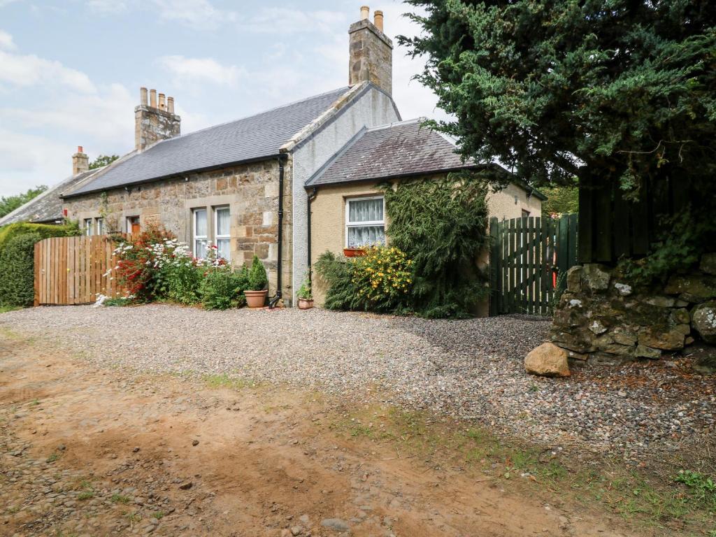 uma casa de pedra com uma cerca e uma entrada de cascalho em Katmoget Cottage em Cupar