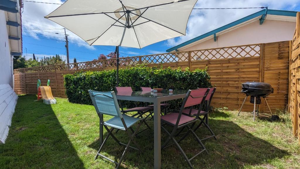 einen Tisch und Stühle mit einem Sonnenschirm und einem Grill in der Unterkunft Andernos-Maison de centre-ville avec jardin in Andernos-les-Bains