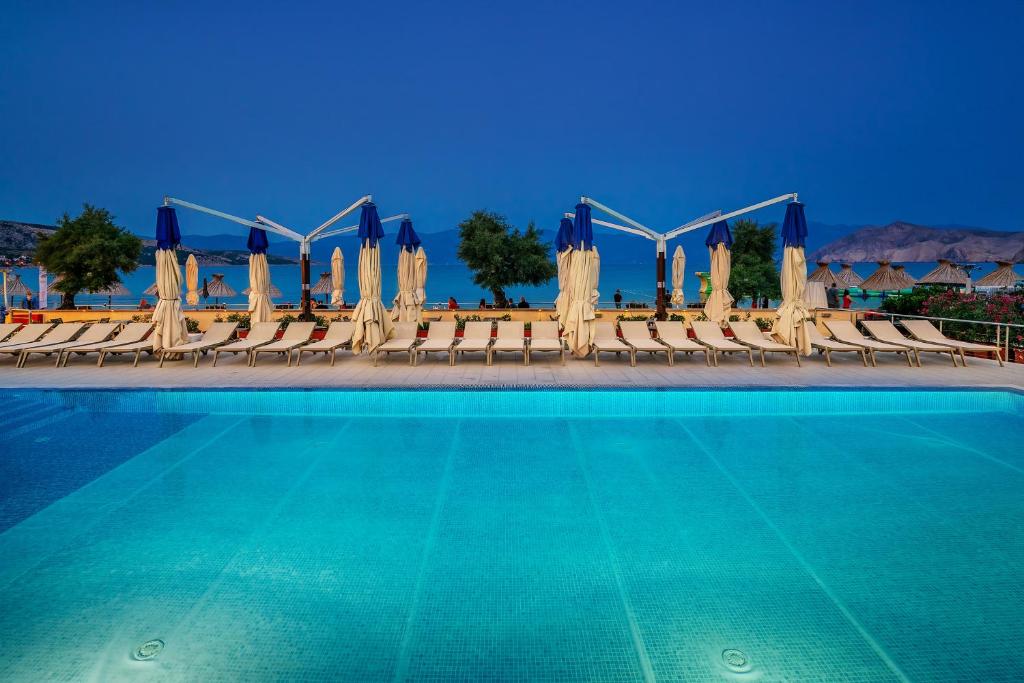 a swimming pool with chairs and umbrellas at Hotel Dobrovit in Baška