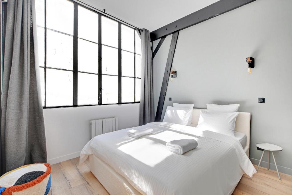 a bedroom with a bed with white sheets and windows at GemBnB Luxury Apartments - Sedaine in Paris