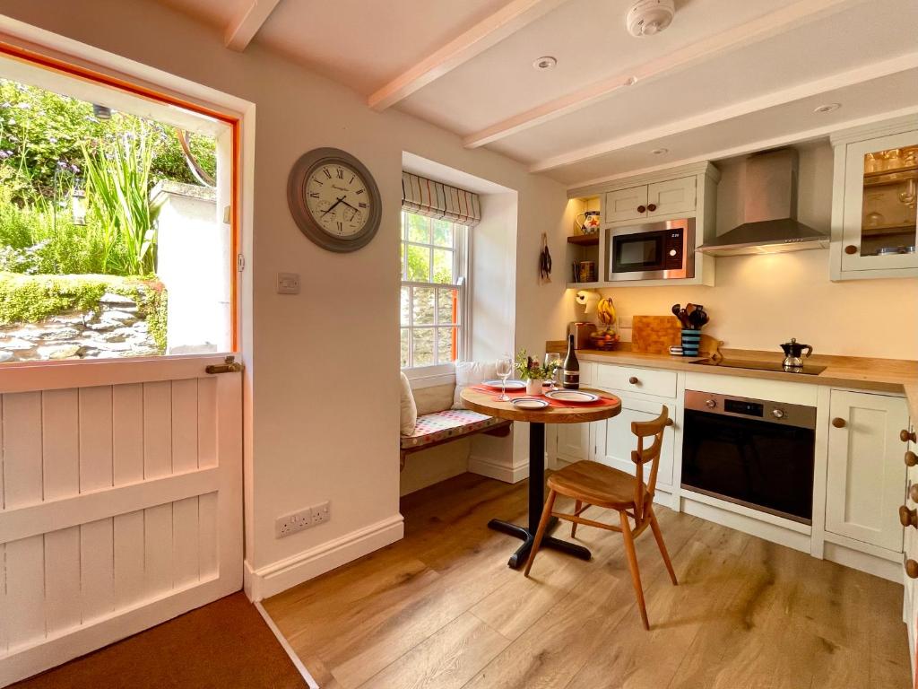 a kitchen with a table and a clock on the wall at Just Opened. Romantic Clifftop Retreat in Portloe
