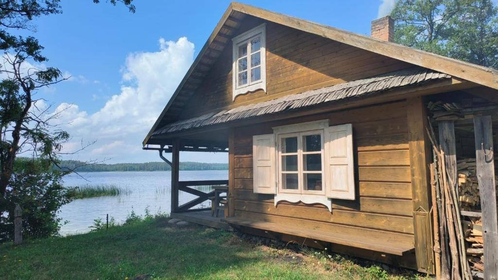 una pequeña casa de madera con una ventana y un cuerpo de agua en Lakefront Log House and Sauna, en Ginučiai