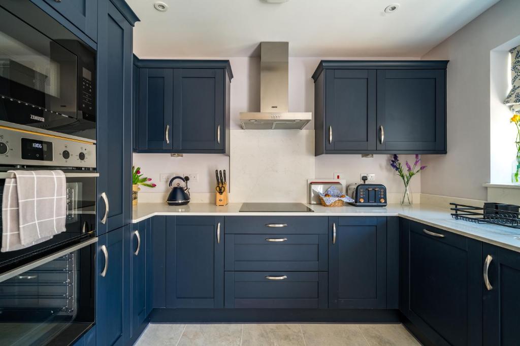 uma cozinha com armários azul marinho e bancadas brancas em Fleming Cottage - Contemporary Cotswold Home 