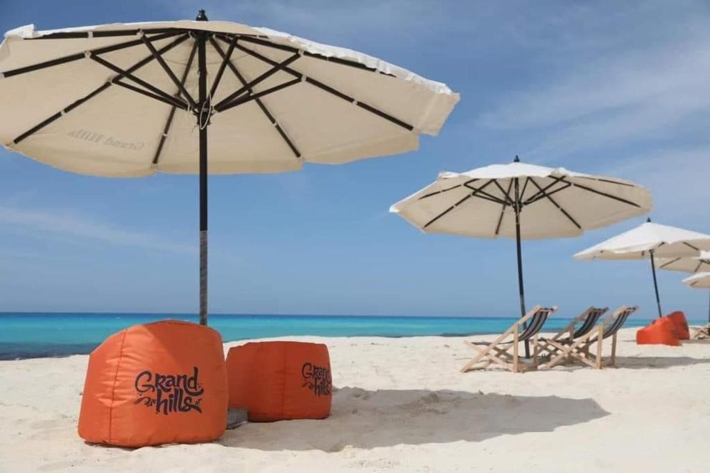 two umbrellas and chairs on a beach with the ocean at Challete 3 rooms , Air conditioned , grand Hills , north coast in El Hamam
