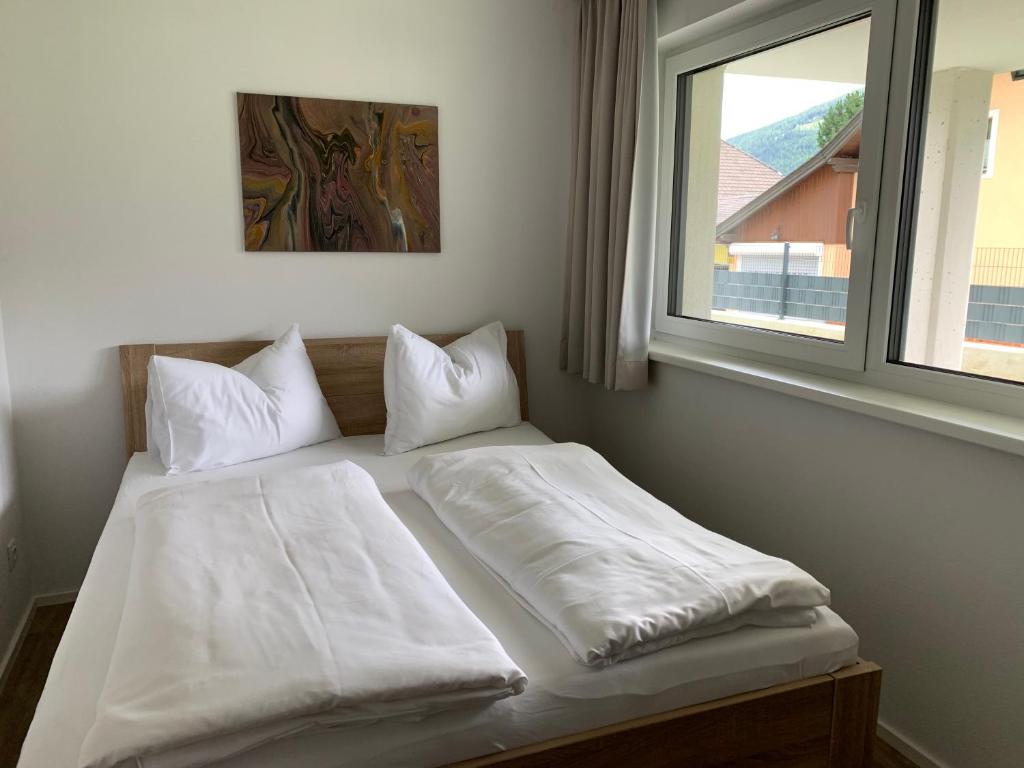łóżko z białą pościelą i poduszkami obok okna w obiekcie Ferienwohnung Siri Zentrum mit Garten w mieście Sankt Michael im Lungau