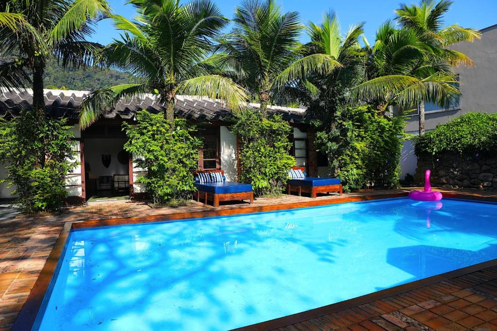 a large swimming pool with two chairs and palm trees at Canto das Laranjeiras Beach Club Guaiuba in Guarujá