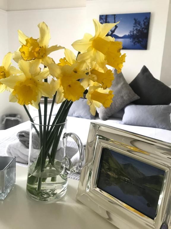 a vase of yellow flowers sitting next to a picture frame at Roses Cottage - near Scafell Comfy Modern Idyllic in Santon Bridge