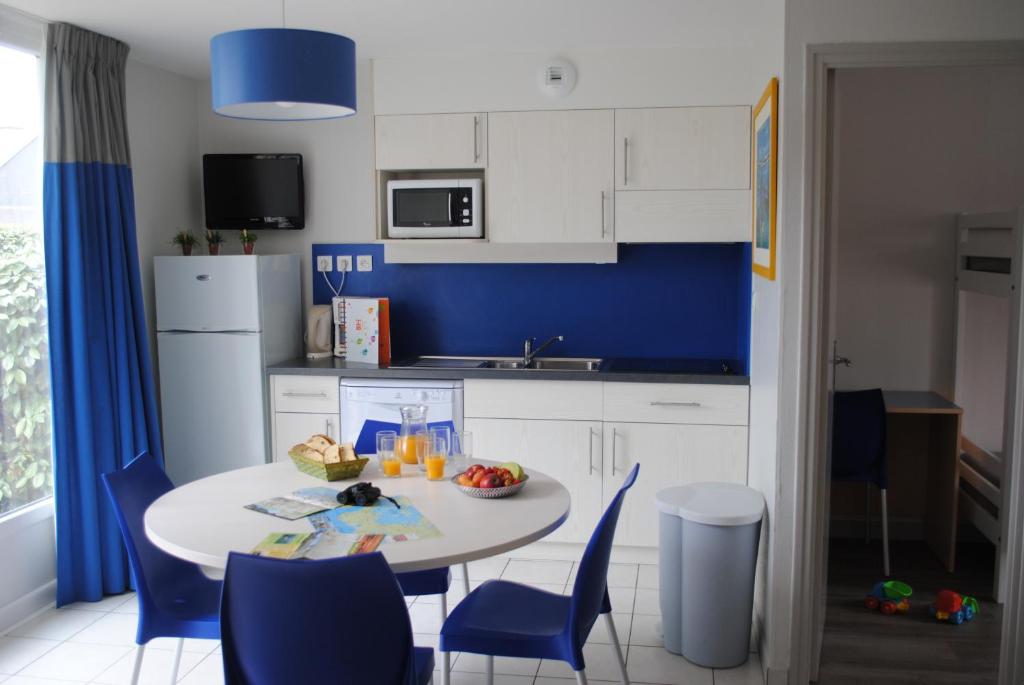 une cuisine avec une table et des chaises et un mur bleu dans l'établissement VVF Golfe du Morbihan Sarzeau Arzon, à Sarzeau