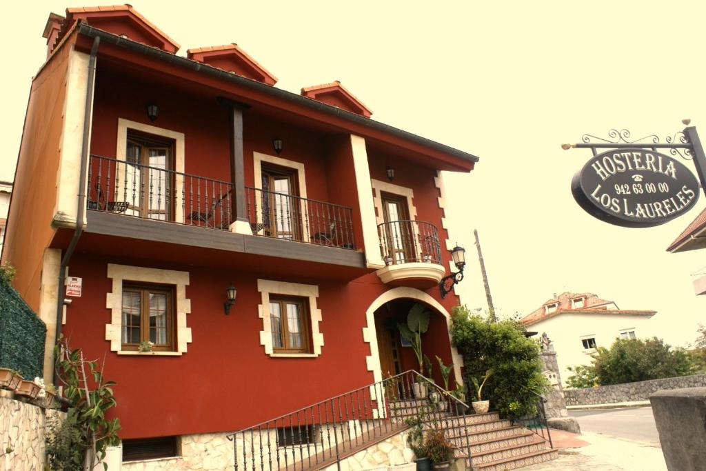 a red building with a balcony on a street at Hosteria Los Laureles in Noja