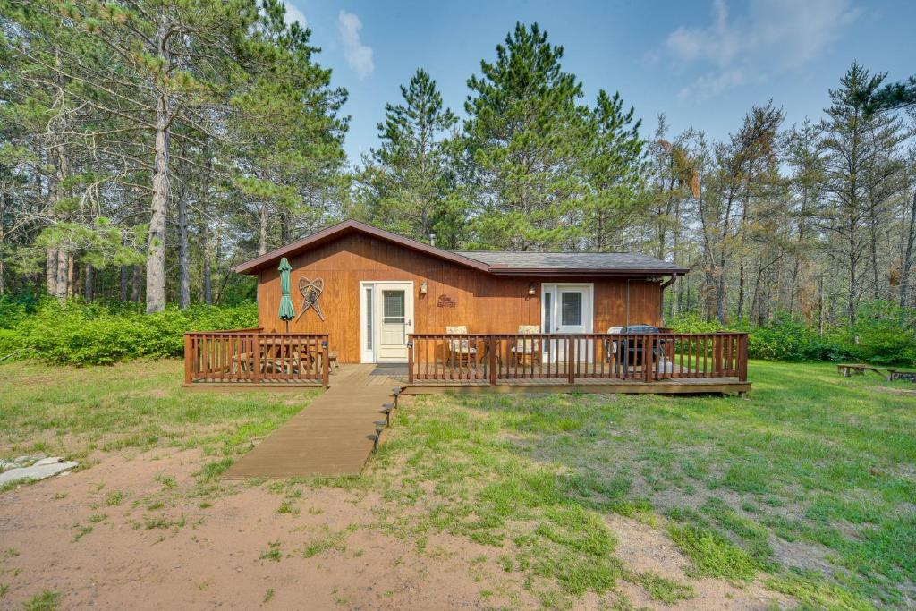 a small cabin with a large deck in the woods at Woodland Cabin with Fishing, ATV and Snowmobile Trails in Lake Nebagamon