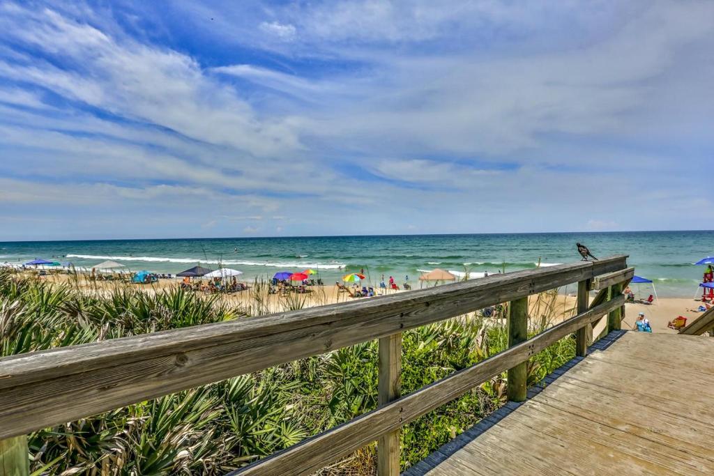 um calçadão de madeira que leva a uma praia com pessoas e guarda-sóis em Stunning 2 Bedroom 2 Bath Oceanwalk Condo em New Smyrna Beach