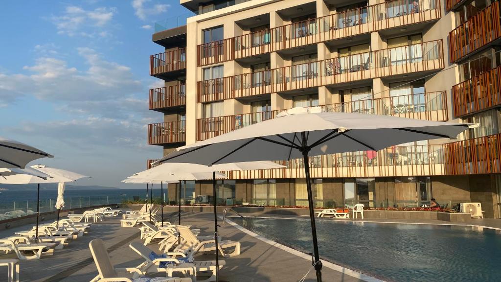 a pool with chairs and umbrellas in front of a building at PARADISO 402 Private Apartment Nessebar in Nesebar