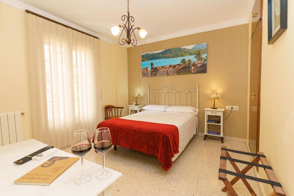 Hotel Colón في روندا: غرفة في الفندق مع سرير وطاولة مع كؤوس للنبيذ
