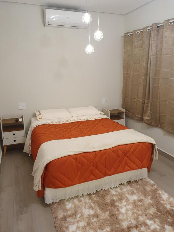 a bedroom with a large bed with an orange blanket at Villa Ida, Suíte 01 c/ copa p/ casal in Serra Negra
