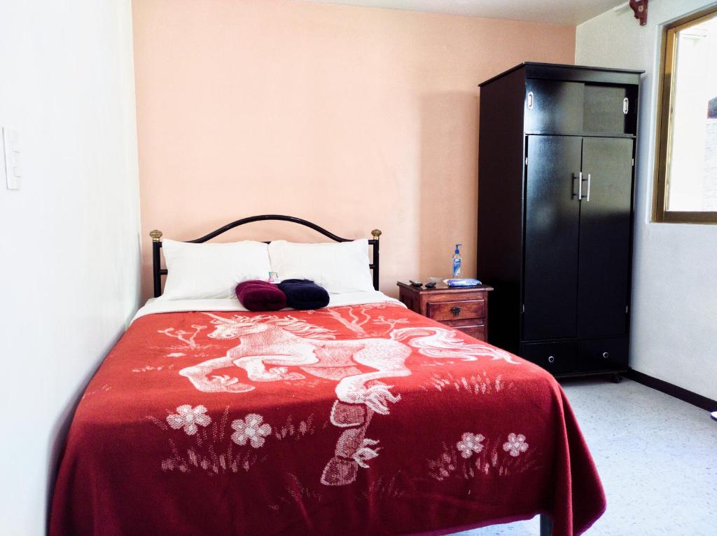 a bedroom with a bed with a red blanket and a black cabinet at Cómoda habitación doble 5 min del Aeropuerto CDMX in Mexico City