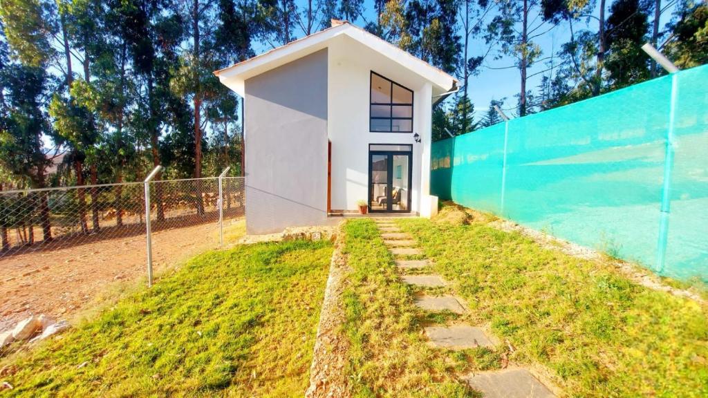 ein kleines weißes Haus auf einem Hügel neben einem Zaun in der Unterkunft Casa de Campo Mirador de la Retama in Cajamarca