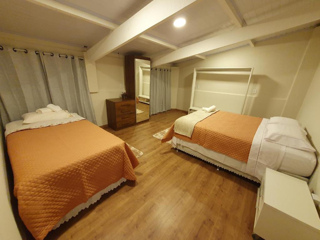 2 Betten befinden sich in einem Zimmer mit Holzböden. in der Unterkunft Villa Ida Acomodações, 3 suítes aconchegantes e charmosas no centro in Serra Negra