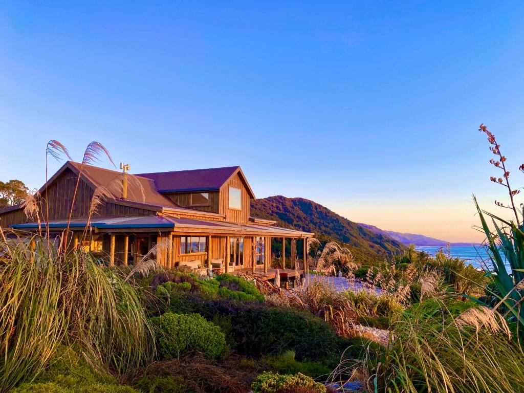 a house on a hill with the ocean in the background at Wild Weka Eco Stay - Off-Grid 4WD RECOMMENDED in Waimarie