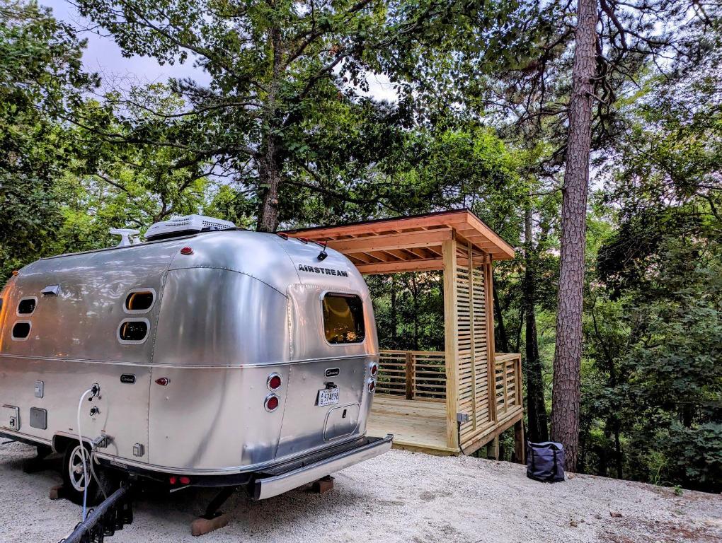 un remolque plateado estacionado junto a una cabaña de madera en Airstream Caravel 2020 Loblolly Pines Adventure Camp en Eureka Springs