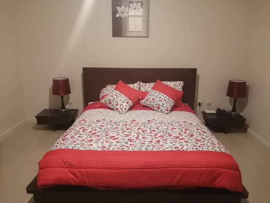 グアヤキルにあるLINDA SUITE Puerto Santa Ana GUAYAQUILのベッド1台(赤と白の枕、ランプ2つ付)
