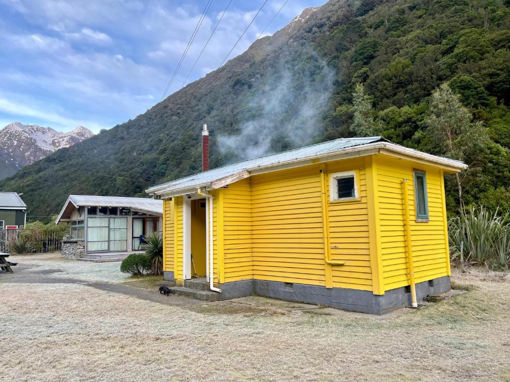 um edifício amarelo em frente a uma montanha em Basic, Super 'Cosy' Cabin in The Middle of National Park and Mountains em Otira