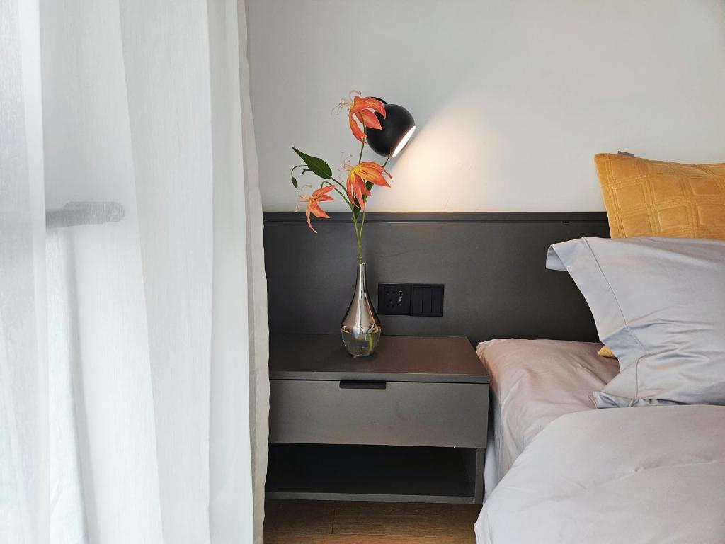 a vase with orange flowers on a table next to a bed at base-Beijing Wangfujing Serviced Apartment- in Hutong &Bike rental &Close to Forbidden City, Tian'anmen Square &Subway nearby &Free coffee &Washing machine,Kitchen &Restaurant discount &English speaking &High speed free WiFi in Beijing