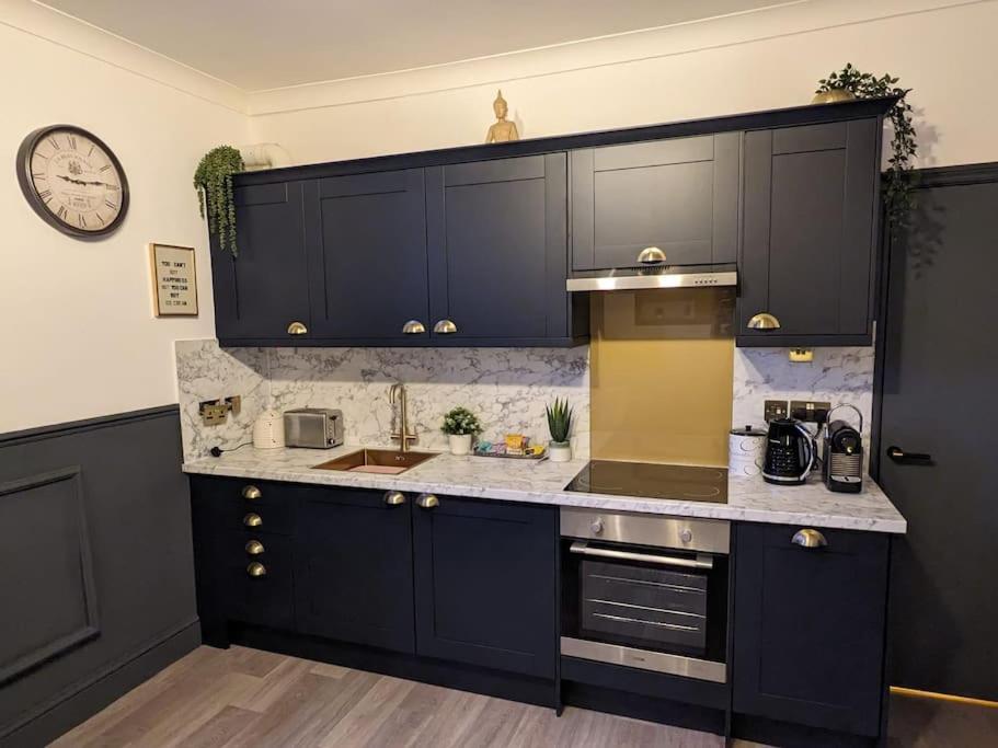 een keuken met zwarte kasten en een klok aan de muur bij St Davids Central Apartment in Exeter