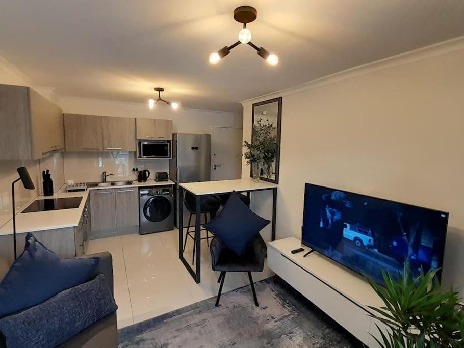 a living room with a large tv and a kitchen at Modern Apartment in Chapel Towers (with Inverter) in Cape Town