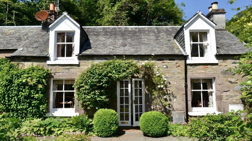 an old stone house with white windows and bushes at Glen Cottage in Comrie