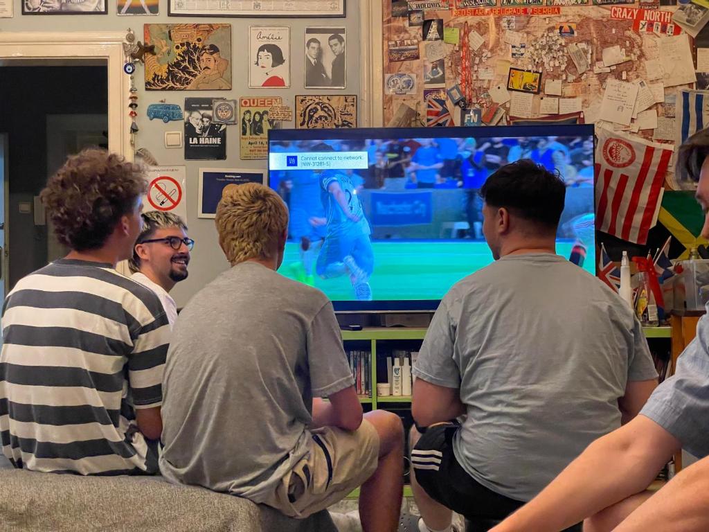 um grupo de homens sentados num sofá a jogar um jogo de vídeo em Habitat Hostel em Belgrado