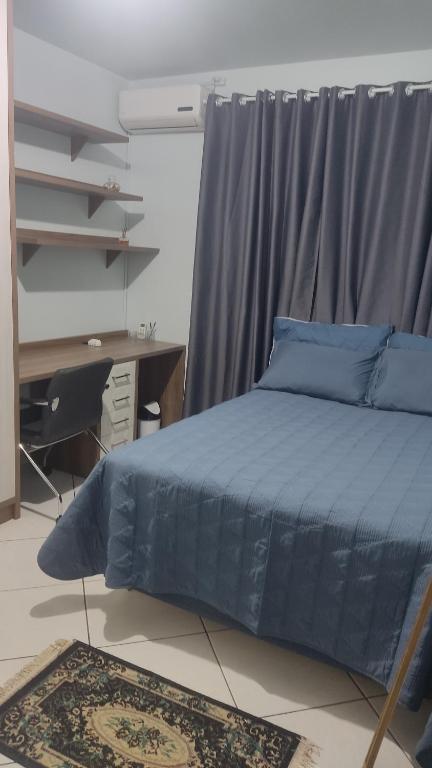 een slaapkamer met een blauw bed en een bureau bij Aconchego in Chapecó