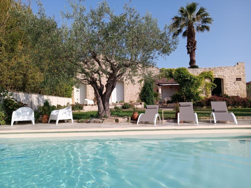 uma piscina com cadeiras e árvores e uma casa em Maison de Charme - Maréchalerie - Nîmes em Uchaud