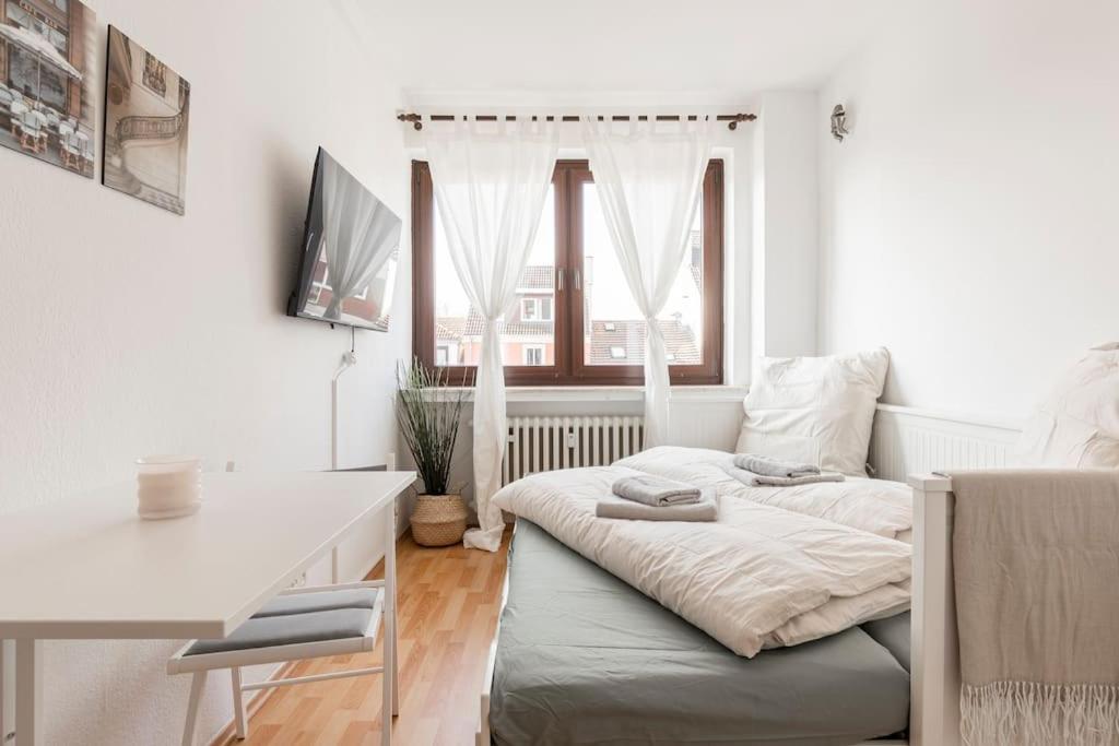 a white bedroom with a bed and a desk and a window at Gemütliches Apartment Neustadt in Bremen