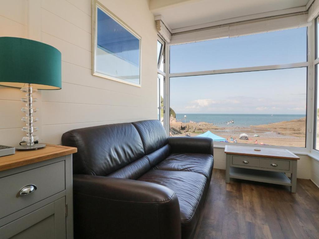 sala de estar con sofá de cuero y vistas al océano en At the Bay Apartment, en Ilfracombe