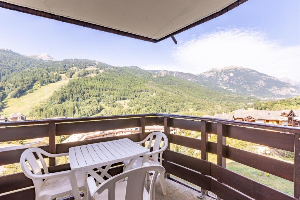 een tafel en 2 stoelen op een balkon met uitzicht op de bergen bij Les Mélèzes - Appt à Serre Chevalier in Saint-Chaffrey